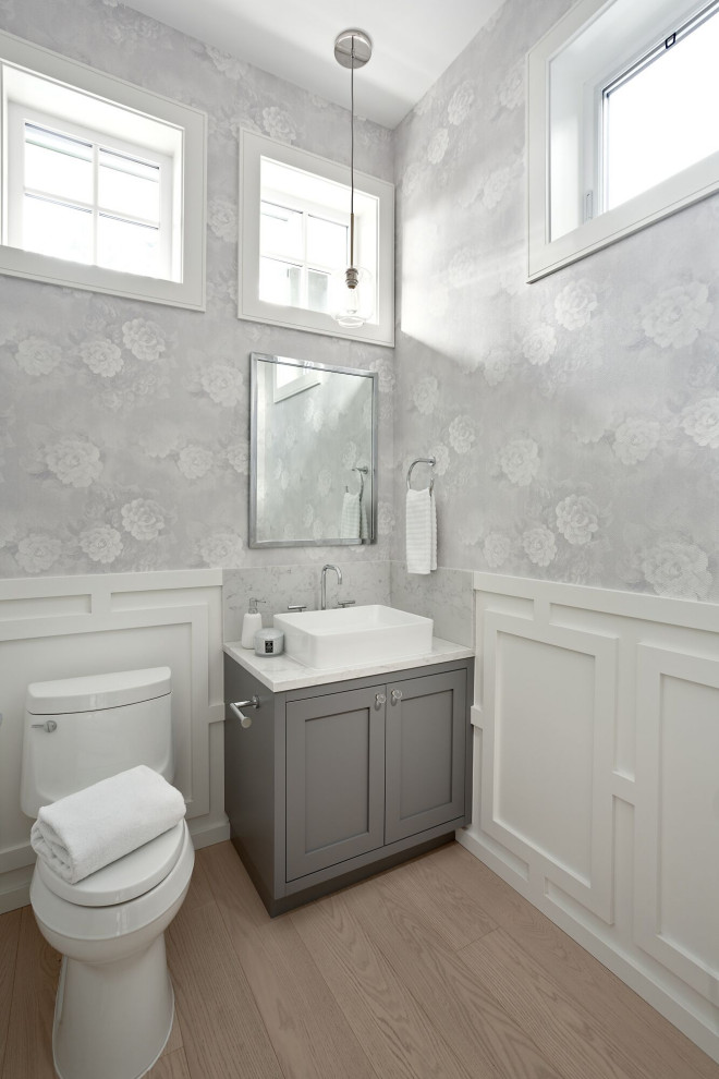 Aménagement d'un petit WC et toilettes classique avec un placard à porte shaker, des portes de placard grises, un mur gris, parquet clair, une vasque, un sol beige, un plan de toilette blanc, meuble-lavabo encastré, boiseries et du papier peint.