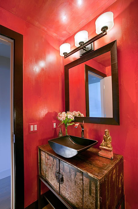 Kleine Asiatische Gästetoilette mit verzierten Schränken, Schränken im Used-Look, roter Wandfarbe, braunem Holzboden, Aufsatzwaschbecken, Waschtisch aus Holz und braunem Boden