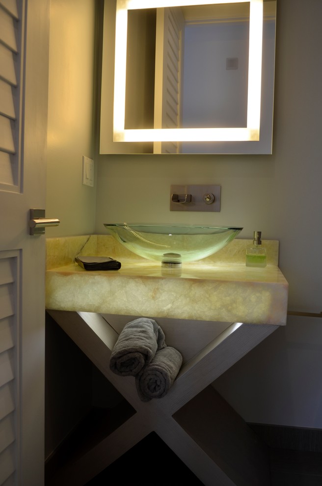 マイアミにあるラグジュアリーな小さなコンテンポラリースタイルのおしゃれなトイレ・洗面所 (ベッセル式洗面器、オープンシェルフ、グレーのキャビネット、オニキスの洗面台、一体型トイレ	、グレーの壁) の写真