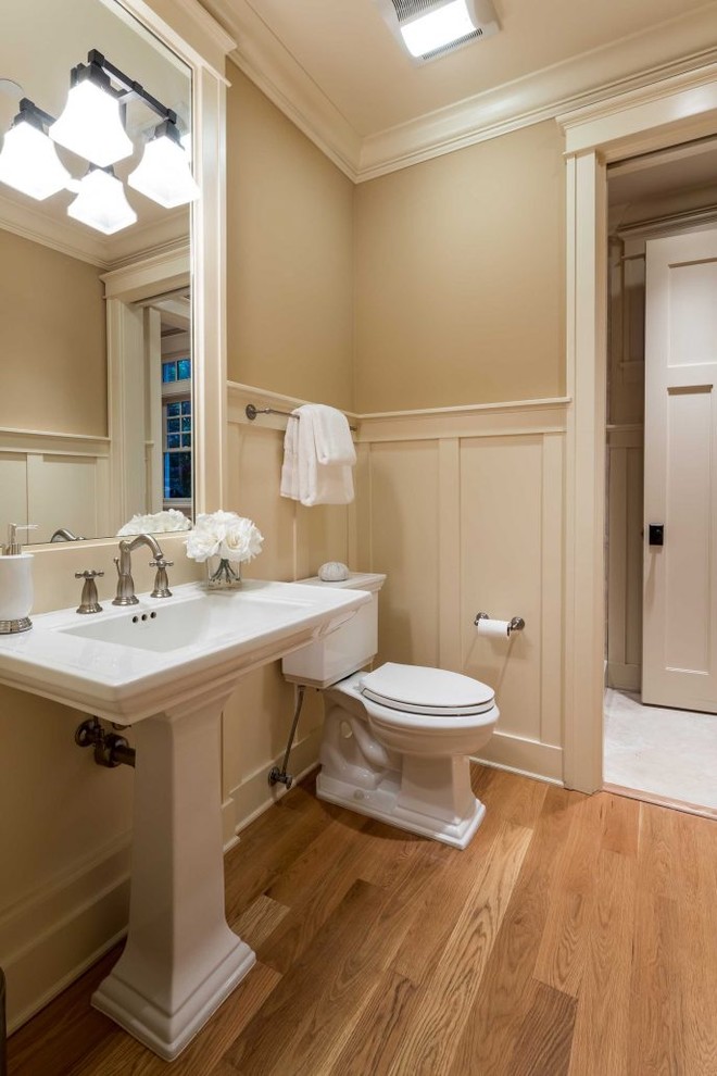 На фото: туалет в классическом стиле с раздельным унитазом, бежевыми стенами, паркетным полом среднего тона, раковиной с пьедесталом и коричневым полом с