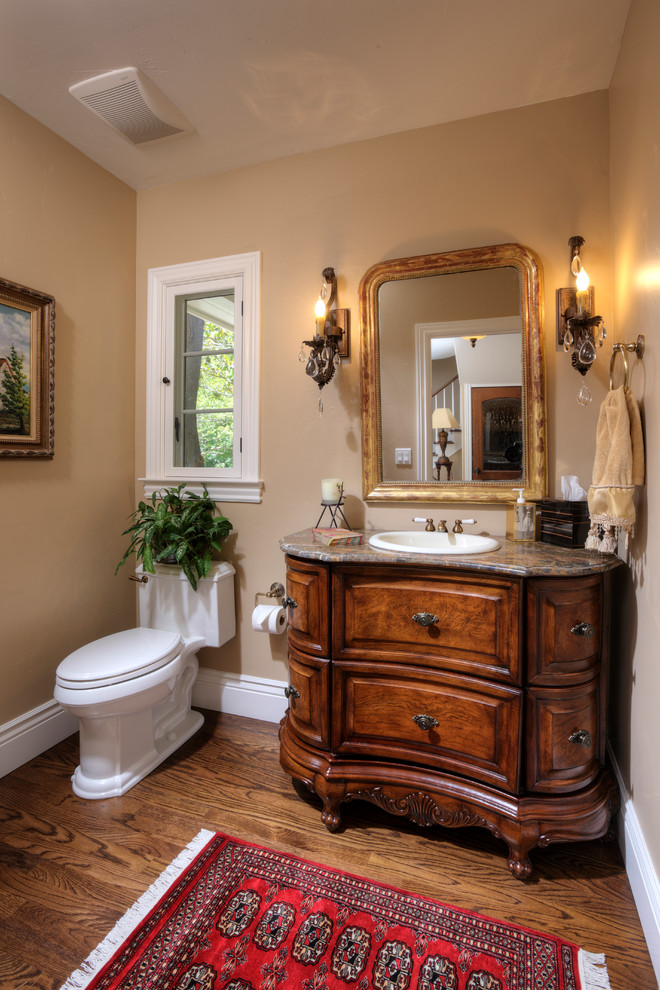 Example of a small classic medium tone wood floor powder room design in Sacramento with furniture-like cabinets, dark wood cabinets, marble countertops, a one-piece toilet, a drop-in sink and beige walls