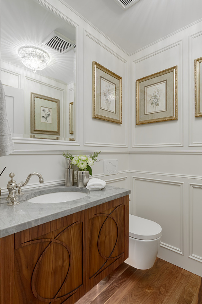 Exempel på ett klassiskt grå grått toalett, med möbel-liknande, bruna skåp, en vägghängd toalettstol, vita väggar, mellanmörkt trägolv, bänkskiva i kvartsit och brunt golv