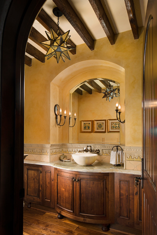 Exemple d'un grand WC et toilettes méditerranéen en bois foncé avec un placard en trompe-l'oeil, un carrelage beige, un carrelage gris, un mur jaune, un sol en bois brun, une vasque et un plan de toilette en marbre.