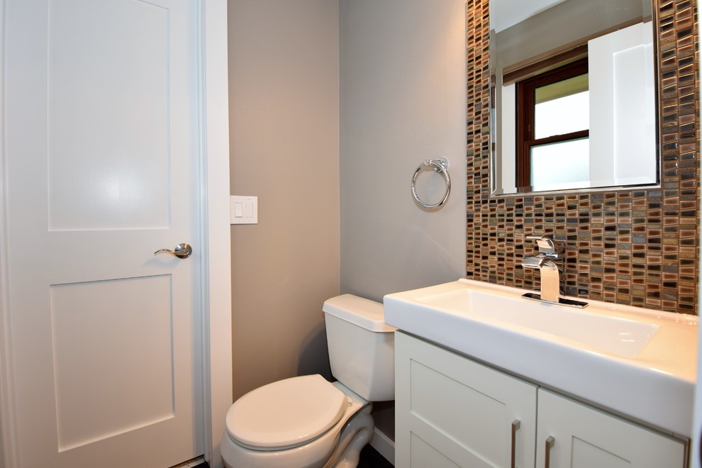 Medelhavsstil inredning av ett mellanstort toalett, med skåp i shakerstil, vita skåp, en toalettstol med separat cisternkåpa, mosaik, grå väggar, mörkt trägolv, ett integrerad handfat och brunt golv