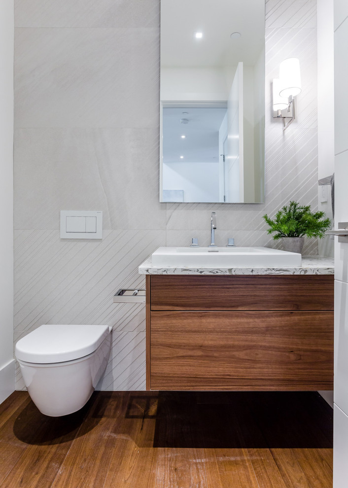 This is an example of a medium sized modern cloakroom in Vancouver with flat-panel cabinets, medium wood cabinets, a wall mounted toilet, white walls, medium hardwood flooring, a vessel sink and brown floors.