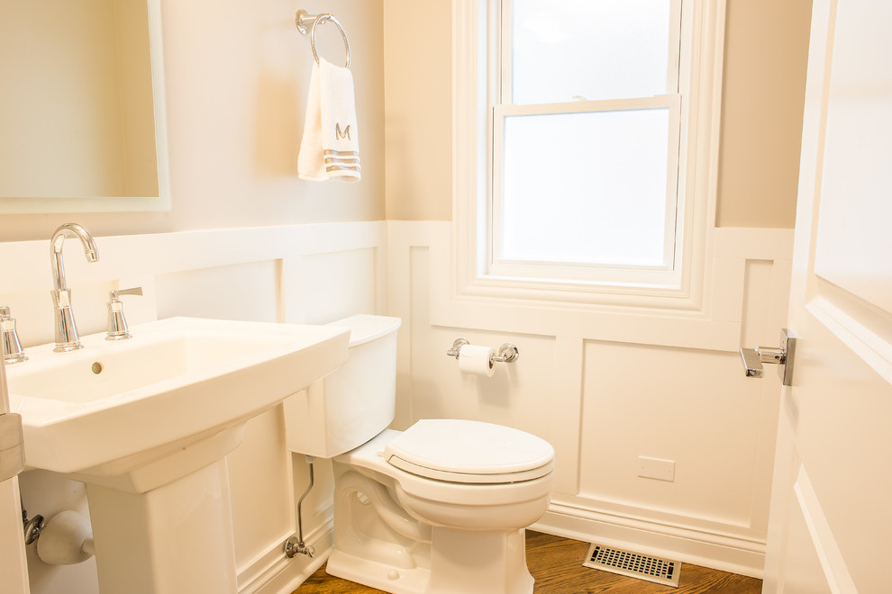 Klassisk inredning av ett litet toalett, med en toalettstol med hel cisternkåpa, beige väggar, mellanmörkt trägolv och ett piedestal handfat