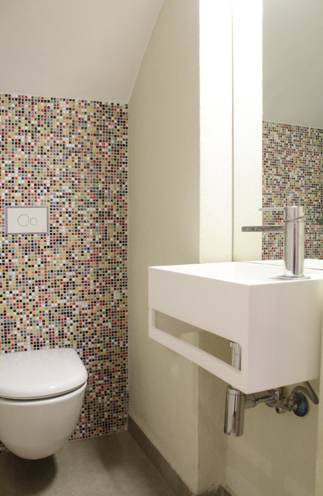 Moderne Gästetoilette mit Wandwaschbecken, farbigen Fliesen, Mosaikfliesen, bunten Wänden und Wandtoilette in Sonstige