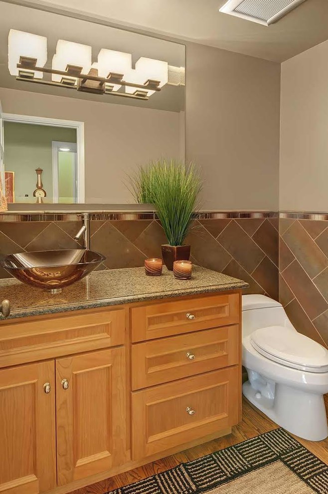 Inredning av ett klassiskt mellanstort grå grått toalett, med luckor med infälld panel, en toalettstol med hel cisternkåpa, beige kakel, grå väggar, mellanmörkt trägolv, ett fristående handfat, granitbänkskiva och skåp i mellenmörkt trä