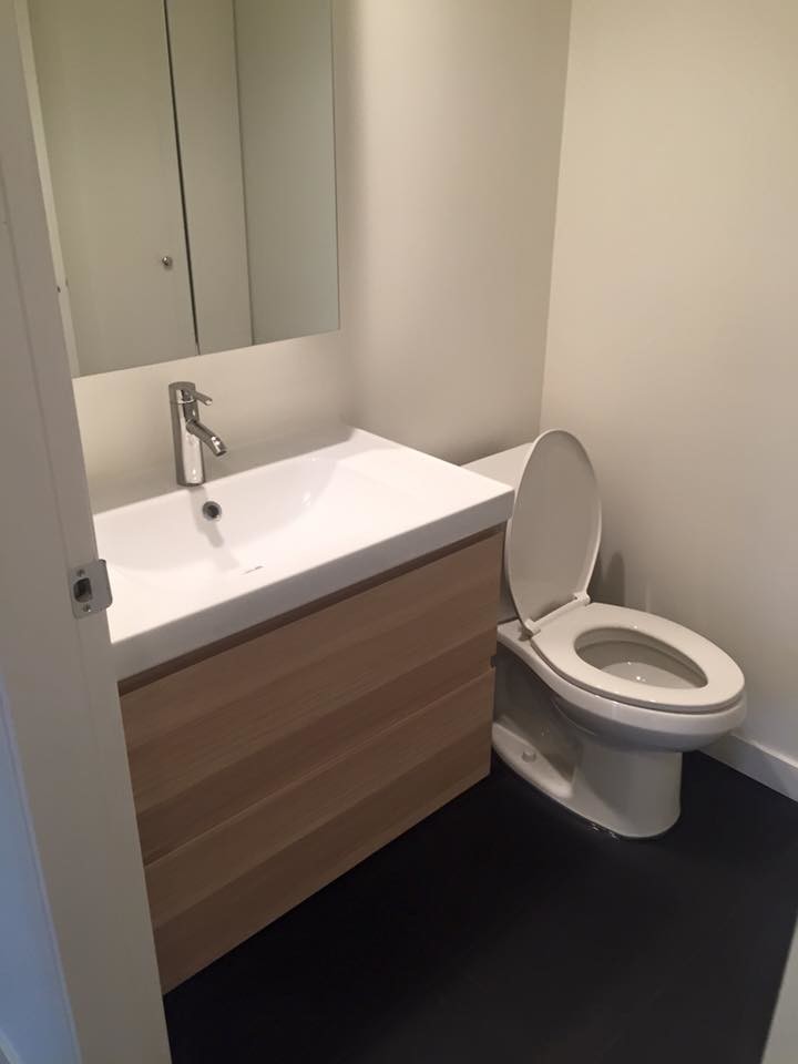 Kleine Moderne Gästetoilette mit flächenbündigen Schrankfronten, hellen Holzschränken, Toilette mit Aufsatzspülkasten, weißer Wandfarbe, Keramikboden, integriertem Waschbecken, Mineralwerkstoff-Waschtisch und schwarzem Boden in Vancouver