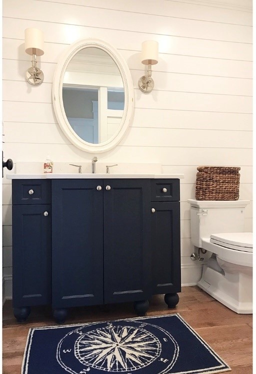 Cette photo montre un petit WC et toilettes bord de mer avec un placard avec porte à panneau encastré, des portes de placard bleues, un mur blanc, un sol en bois brun et un plan de toilette en quartz.