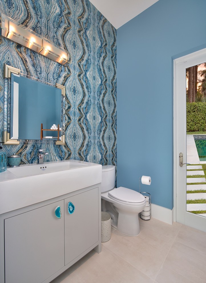 マイアミにある中くらいなコンテンポラリースタイルのおしゃれなトイレ・洗面所 (フラットパネル扉のキャビネット、白いキャビネット、分離型トイレ、マルチカラーのタイル、セラミックタイル、青い壁、セラミックタイルの床、アンダーカウンター洗面器、人工大理石カウンター、白い床、白い洗面カウンター) の写真