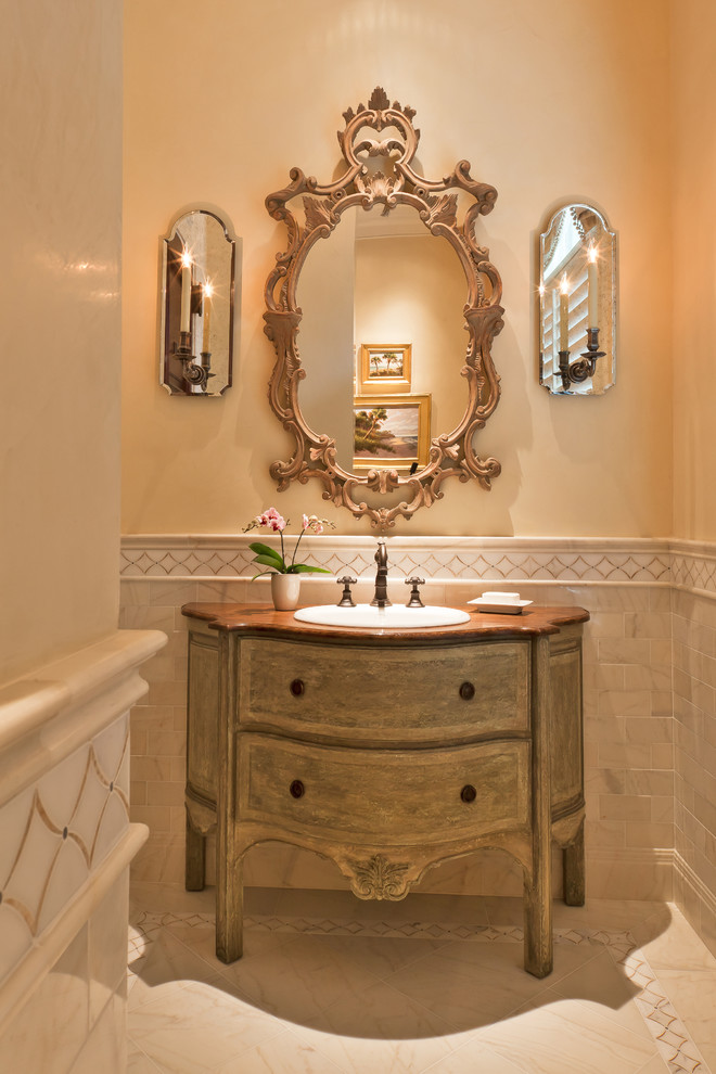 На фото: туалет в классическом стиле с накладной раковиной, фасадами островного типа, бежевой плиткой, бежевыми стенами и светлыми деревянными фасадами с