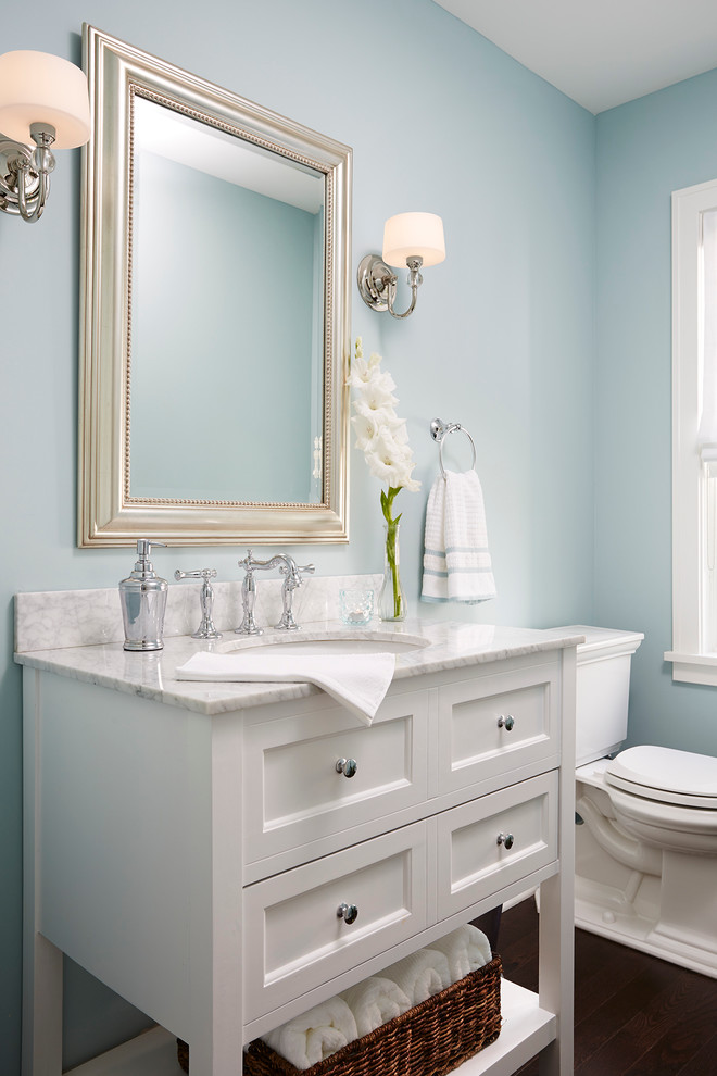 Exempel på ett mellanstort klassiskt vit vitt toalett, med ett undermonterad handfat, vita skåp, blå väggar, en toalettstol med separat cisternkåpa, stenhäll, mörkt trägolv, marmorbänkskiva och luckor med infälld panel