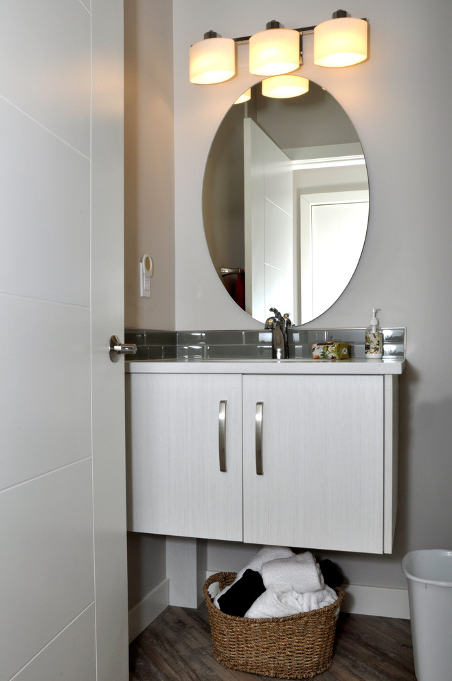 Immagine di un piccolo bagno di servizio minimal con ante lisce, ante bianche, WC a due pezzi, piastrelle grigie, piastrelle di vetro, pareti grigie, pavimento in vinile e lavabo sottopiano