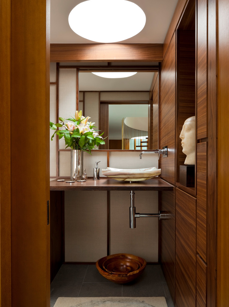 Mittelgroße Moderne Gästetoilette mit Aufsatzwaschbecken, hellbraunen Holzschränken, Waschtisch aus Holz, flächenbündigen Schrankfronten, Schieferboden und brauner Waschtischplatte in New York