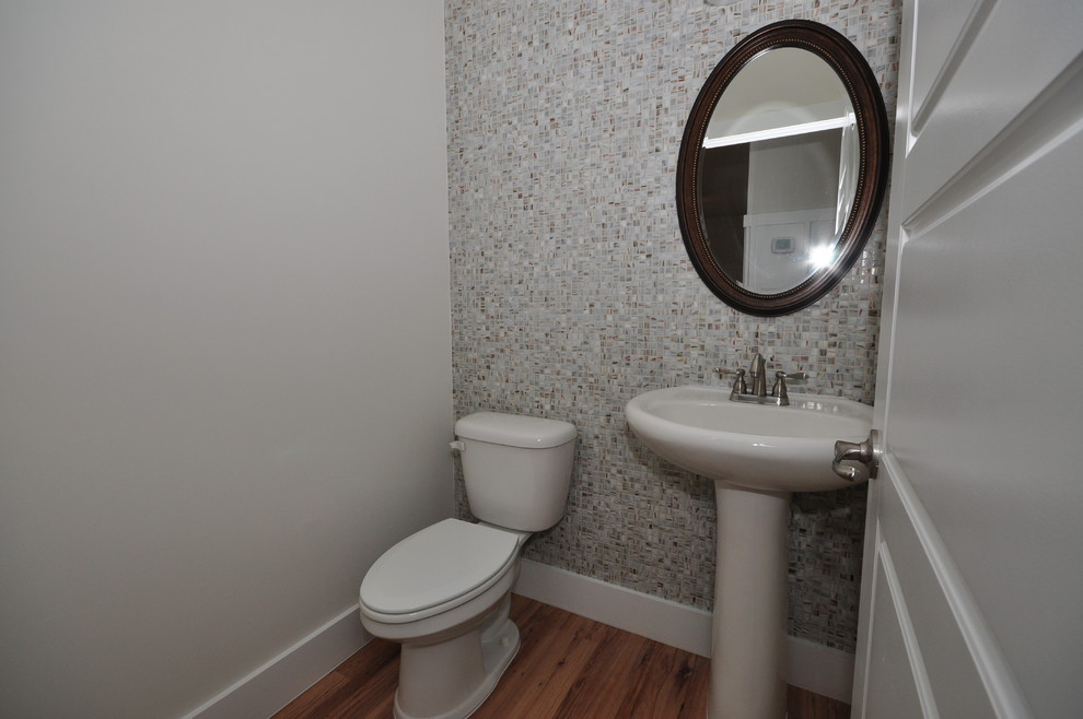Bild på ett mellanstort vintage toalett, med en toalettstol med separat cisternkåpa, grå kakel, mosaik, grå väggar, mellanmörkt trägolv, ett piedestal handfat och brunt golv