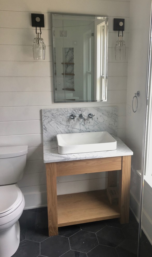This is an example of a small contemporary cloakroom in New York with freestanding cabinets, light wood cabinets, a two-piece toilet, white walls, porcelain flooring, a vessel sink, marble worktops, black floors and grey worktops.