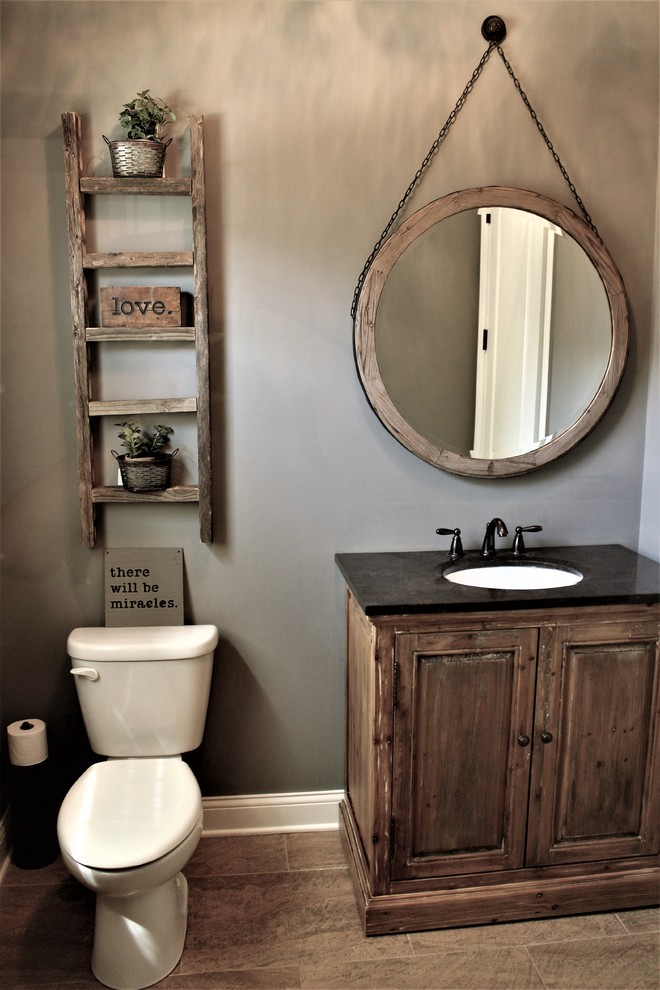 Example of a small mountain style light wood floor and brown floor powder room design in Chicago with raised-panel cabinets, gray walls, an undermount sink, dark wood cabinets, a two-piece toilet and solid surface countertops