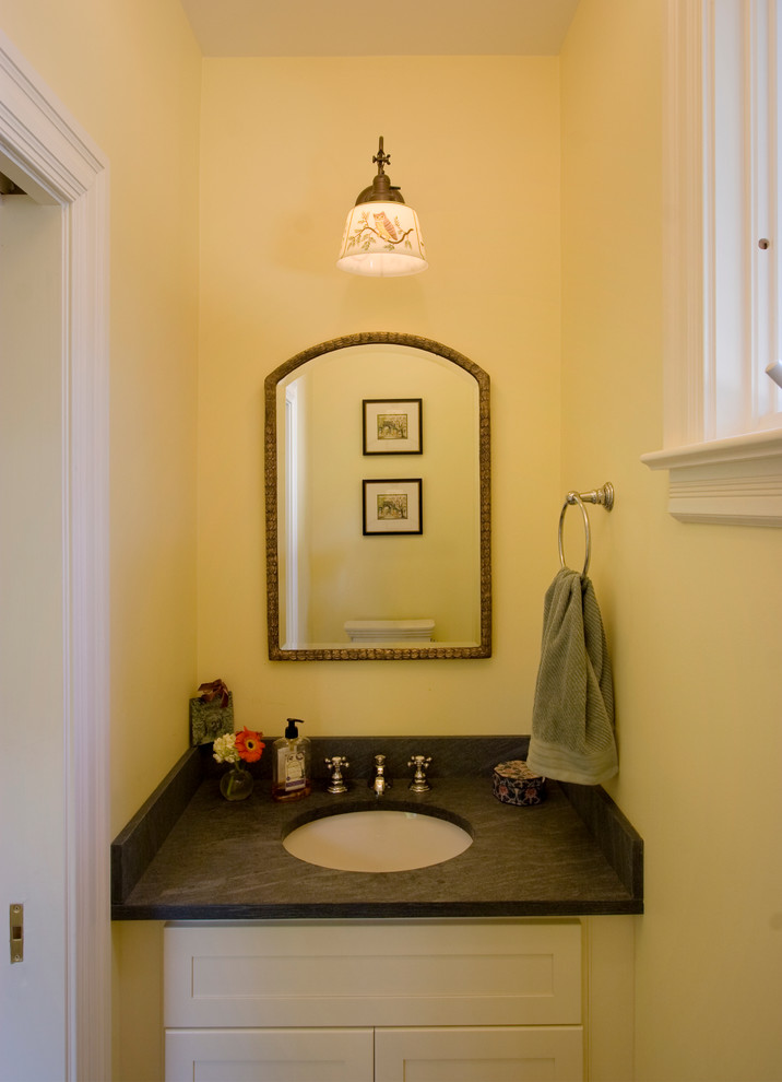 Klassisk inredning av ett litet toalett, med ett undermonterad handfat, skåp i shakerstil, vita skåp, granitbänkskiva, en toalettstol med separat cisternkåpa och gula väggar