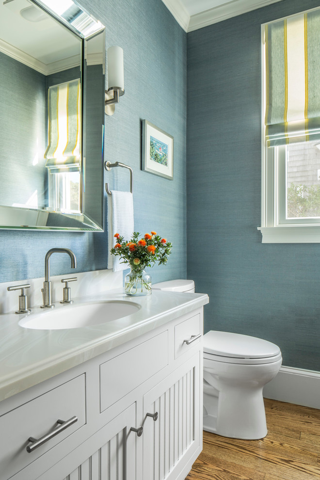 Kleine Maritime Gästetoilette mit weißen Schränken, Toilette mit Aufsatzspülkasten, blauer Wandfarbe, braunem Holzboden und Marmor-Waschbecken/Waschtisch in Boston