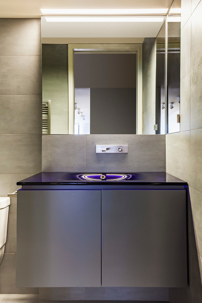 Imagen de aseo minimalista con lavabo suspendido, armarios con paneles lisos, encimera de vidrio y paredes grises