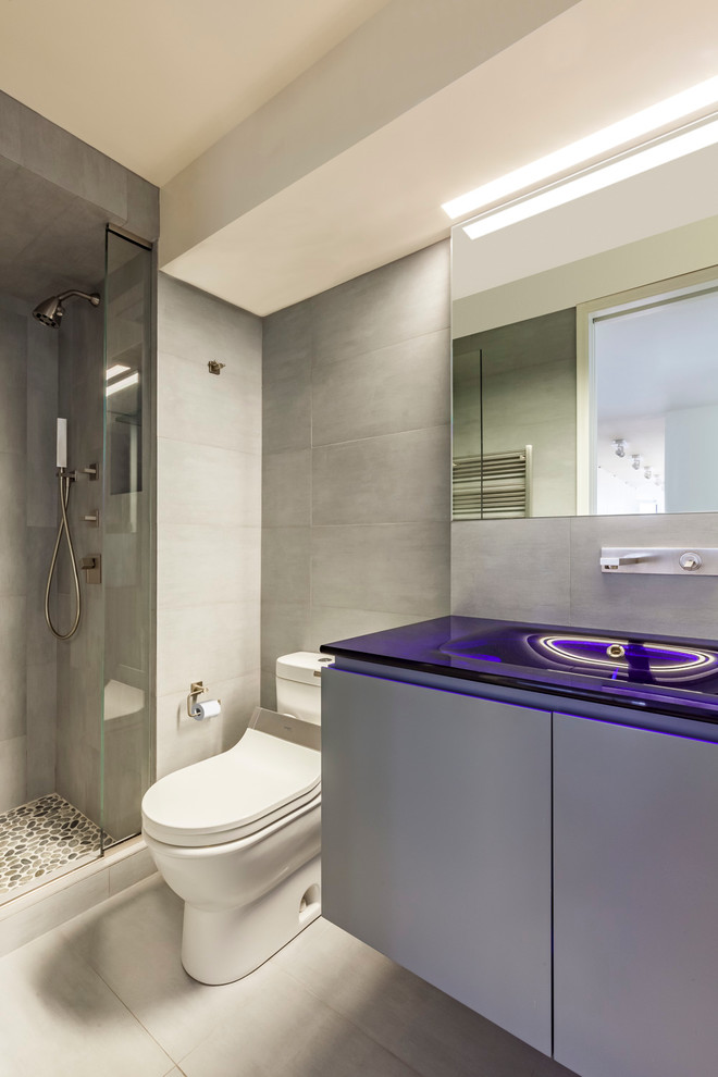 Свежая идея для дизайна: ванная комната в стиле модернизм с подвесной раковиной, плоскими фасадами, стеклянной столешницей, серыми стенами и синей столешницей - отличное фото интерьера