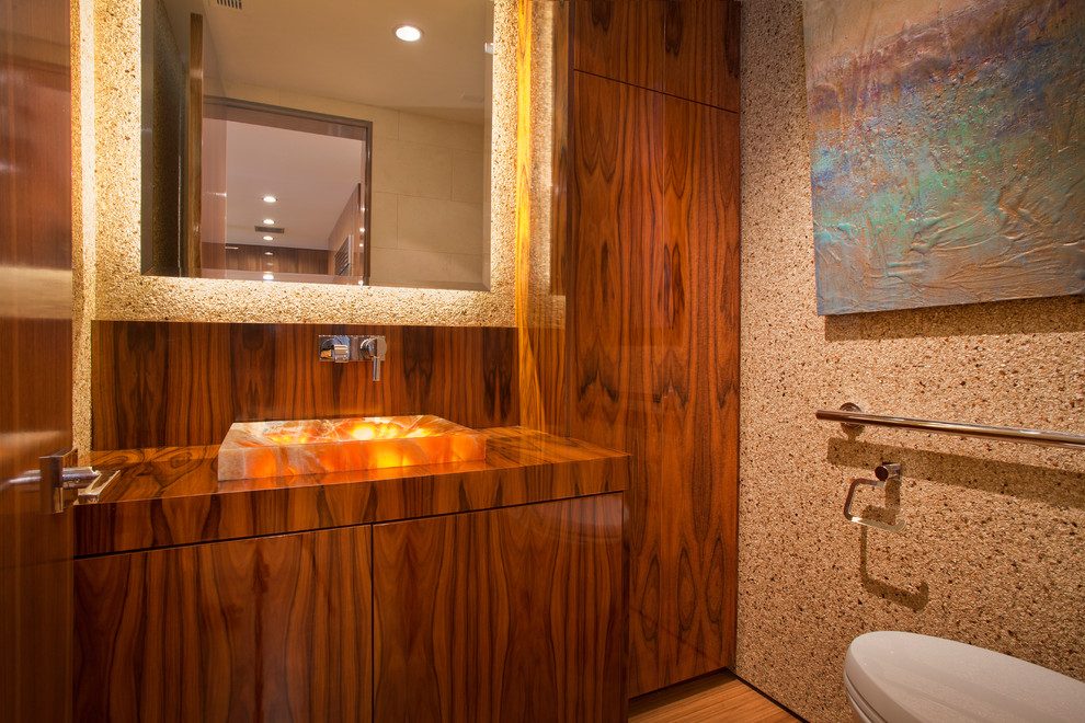 Photo of a medium sized contemporary cloakroom in Orange County with flat-panel cabinets, dark wood cabinets, wooden worktops, a wall mounted toilet, beige walls, light hardwood flooring and a vessel sink.