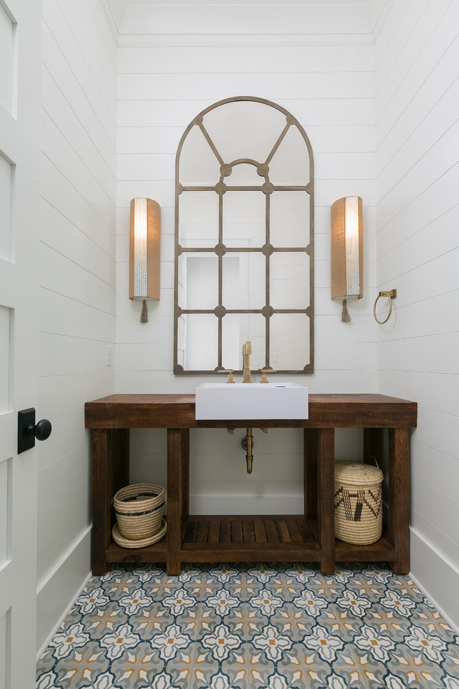 This is an example of a medium sized beach style cloakroom in Charleston with freestanding cabinets, white walls, a vessel sink, wooden worktops, multi-coloured floors, brown worktops, dark wood cabinets and cement flooring.