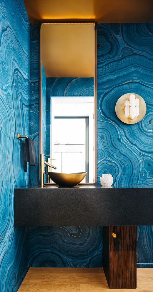 Diseño de aseo actual con puertas de armario de madera en tonos medios, paredes azules, suelo de madera clara y lavabo sobreencimera