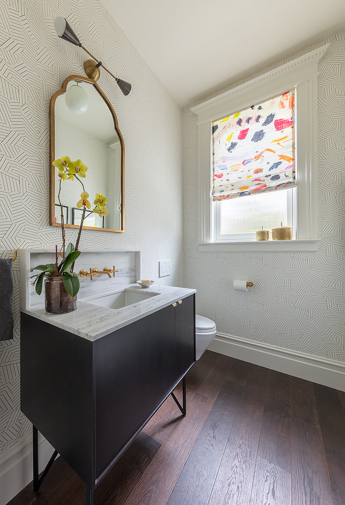 Klassisk inredning av ett vit vitt toalett, med släta luckor, svarta skåp, mörkt trägolv, ett undermonterad handfat och brunt golv