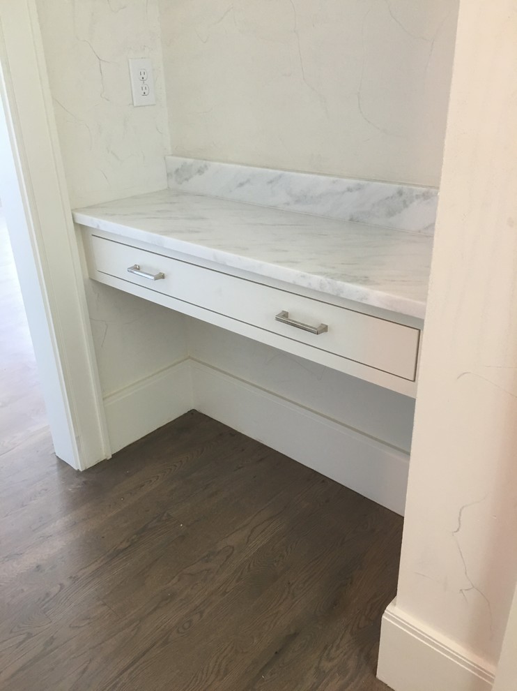 Photo of a medium sized modern cloakroom in Dallas with recessed-panel cabinets, white cabinets, a two-piece toilet, white walls, cement flooring, a submerged sink, marble worktops, grey floors and white worktops.