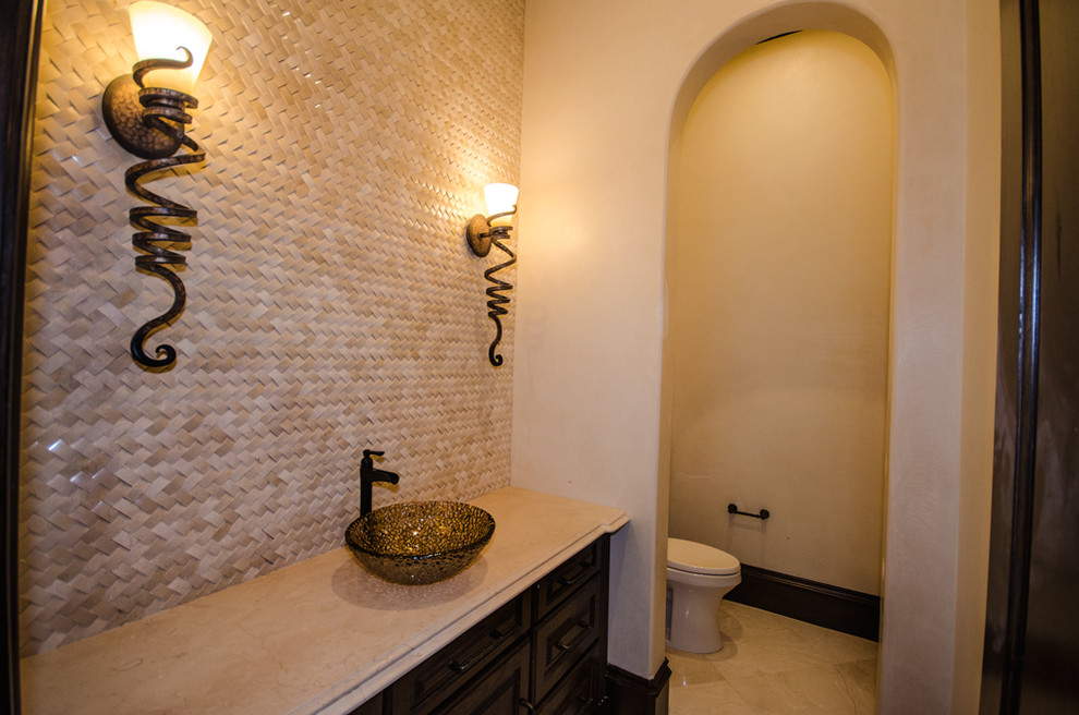 Источник вдохновения для домашнего уюта: огромный туалет в средиземноморском стиле с темными деревянными фасадами, унитазом-моноблоком, бежевой плиткой, плиткой мозаикой, полом из керамогранита, настольной раковиной и столешницей из искусственного кварца