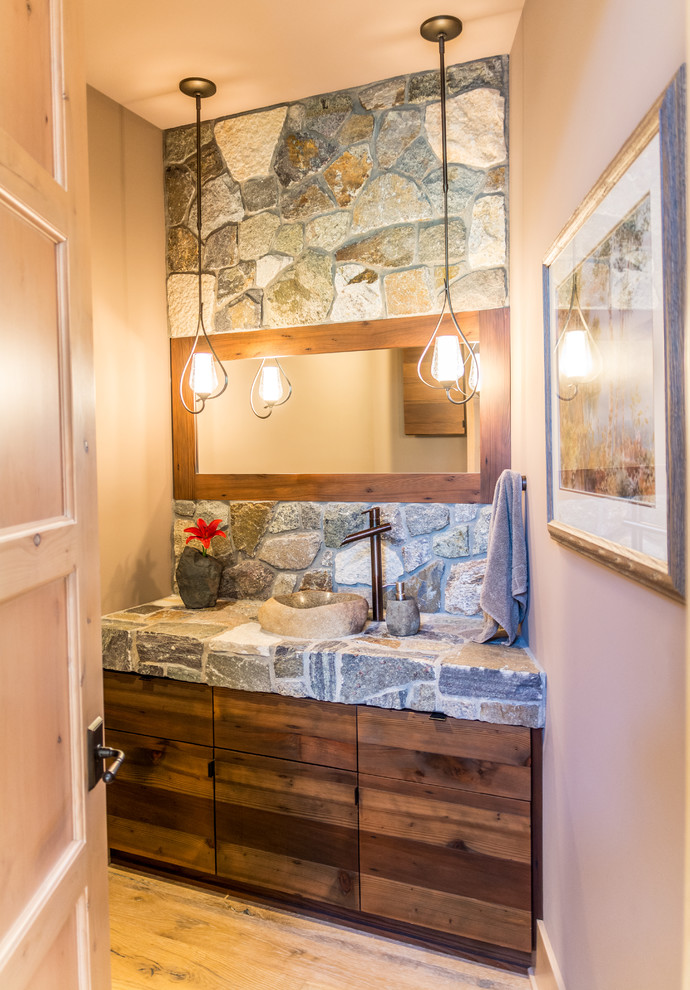 Foto på ett rustikt grå toalett, med släta luckor, skåp i mellenmörkt trä, grå kakel, beige väggar, ljust trägolv, ett fristående handfat och beiget golv