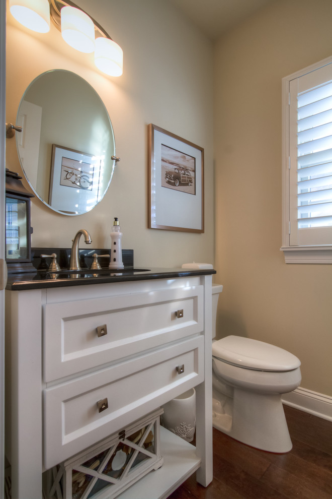 This is an example of a small beach style cloakroom in Philadelphia with recessed-panel cabinets, white cabinets, a two-piece toilet, beige walls, medium hardwood flooring, a submerged sink, quartz worktops and black worktops.