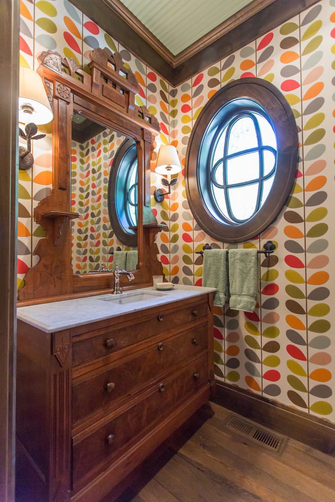 Urige Gästetoilette mit braunen Schränken, farbigen Fliesen, bunten Wänden, braunem Holzboden, integriertem Waschbecken und braunem Boden in Minneapolis