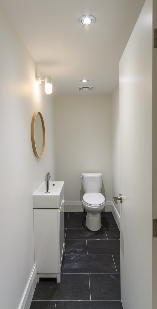Idée de décoration pour un WC et toilettes design de taille moyenne avec un placard à porte plane, des portes de placard blanches, un mur blanc, un sol en ardoise et une vasque.