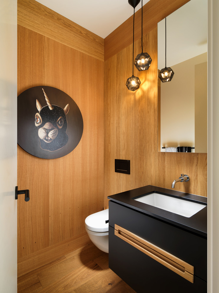 Inspiration pour un WC et toilettes design avec un placard à porte plane, des portes de placard noires, un mur marron, un sol en bois brun, un lavabo encastré, un sol marron et un plan de toilette noir.