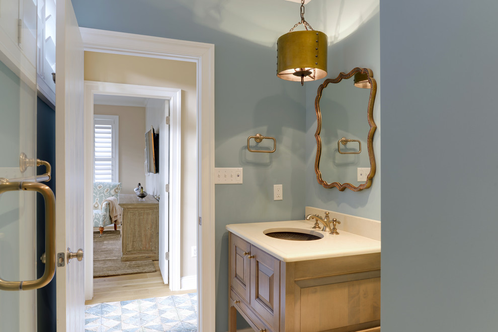 Idee per un bagno di servizio stile marinaro con lavabo sottopiano, ante con bugna sagomata, ante in legno chiaro, top in quarzo composito e pareti blu