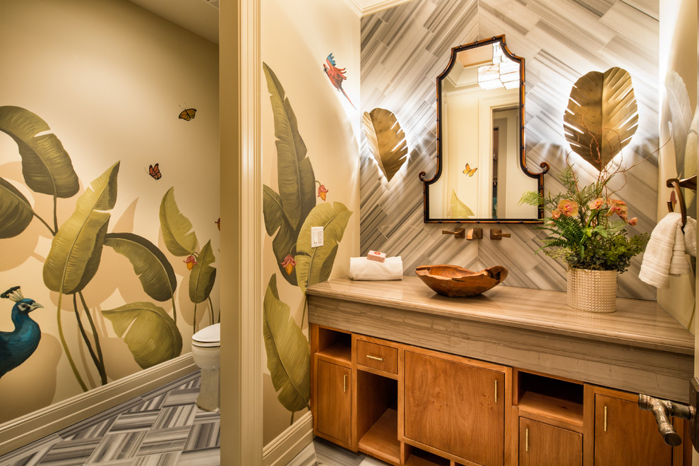 ロサンゼルスにあるトロピカルスタイルのおしゃれなトイレ・洗面所 (フラットパネル扉のキャビネット、中間色木目調キャビネット、マルチカラーの壁、ベッセル式洗面器、ベージュのカウンター、グレーの床) の写真