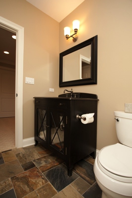 This is an example of a small traditional cloakroom in Chicago with glass-front cabinets, dark wood cabinets, a two-piece toilet, beige walls, slate flooring, a submerged sink, solid surface worktops, brown tiles and grey tiles.