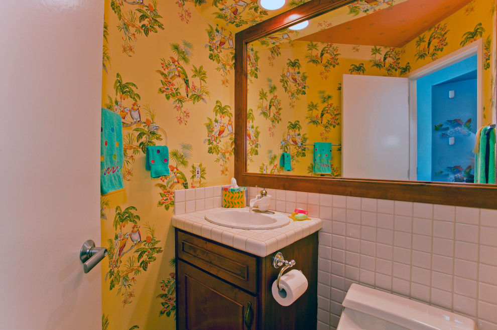 Cette photo montre un petit WC et toilettes exotique en bois foncé avec un lavabo posé, un placard à porte shaker, un plan de toilette en carrelage, WC à poser, un carrelage blanc, des carreaux de céramique et un mur jaune.