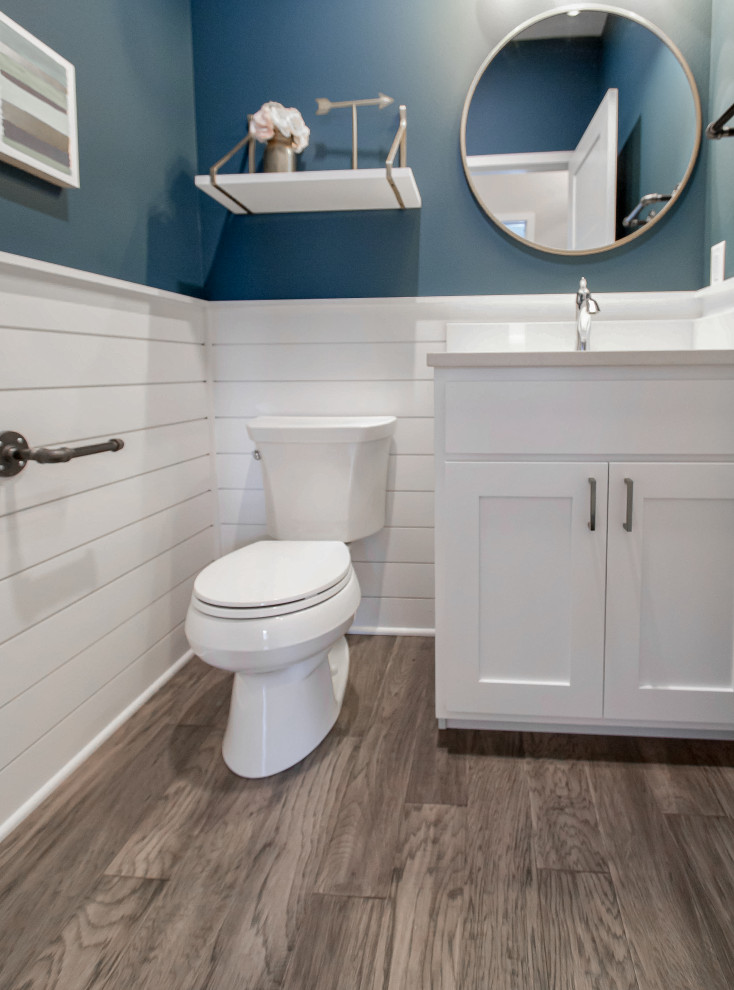 This is an example of a small traditional cloakroom with recessed-panel cabinets, white cabinets, a two-piece toilet, blue tiles, blue walls, medium hardwood flooring, an integrated sink, engineered stone worktops, brown floors and white worktops.