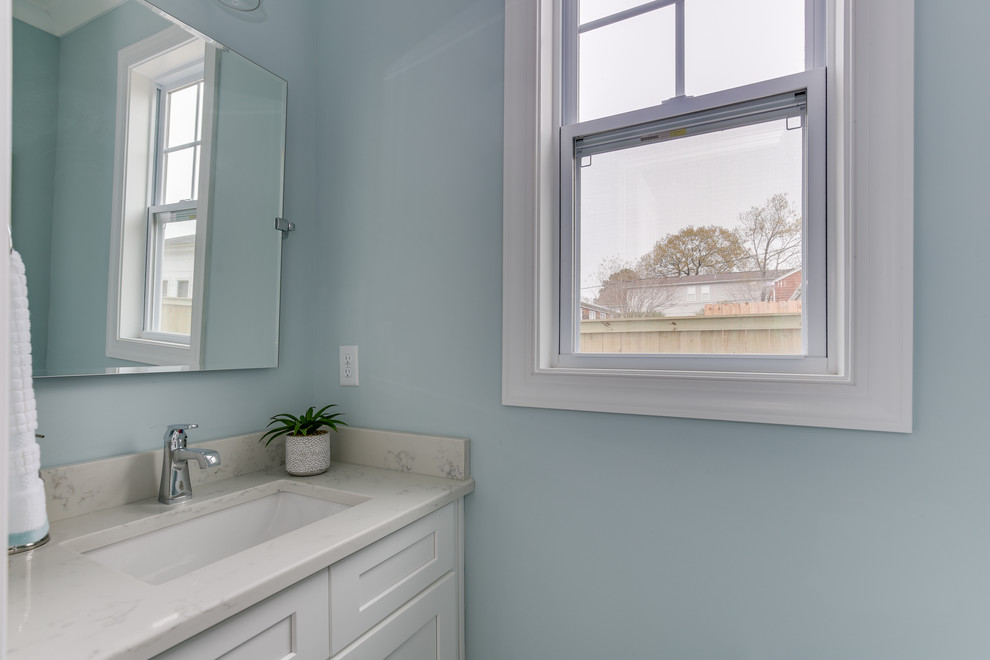 Inspiration for a small coastal cloakroom in Other with shaker cabinets, white cabinets, a one-piece toilet, blue walls, light hardwood flooring, a submerged sink, engineered stone worktops, grey floors and white worktops.