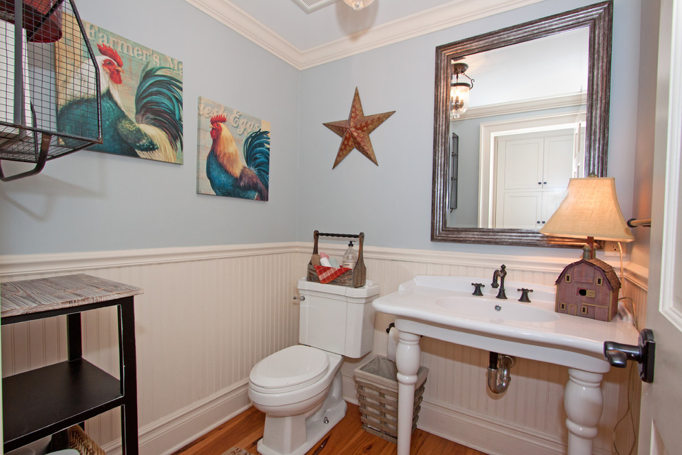 Diseño de aseo de estilo americano con lavabo con pedestal, sanitario de dos piezas, paredes azules y suelo de madera en tonos medios