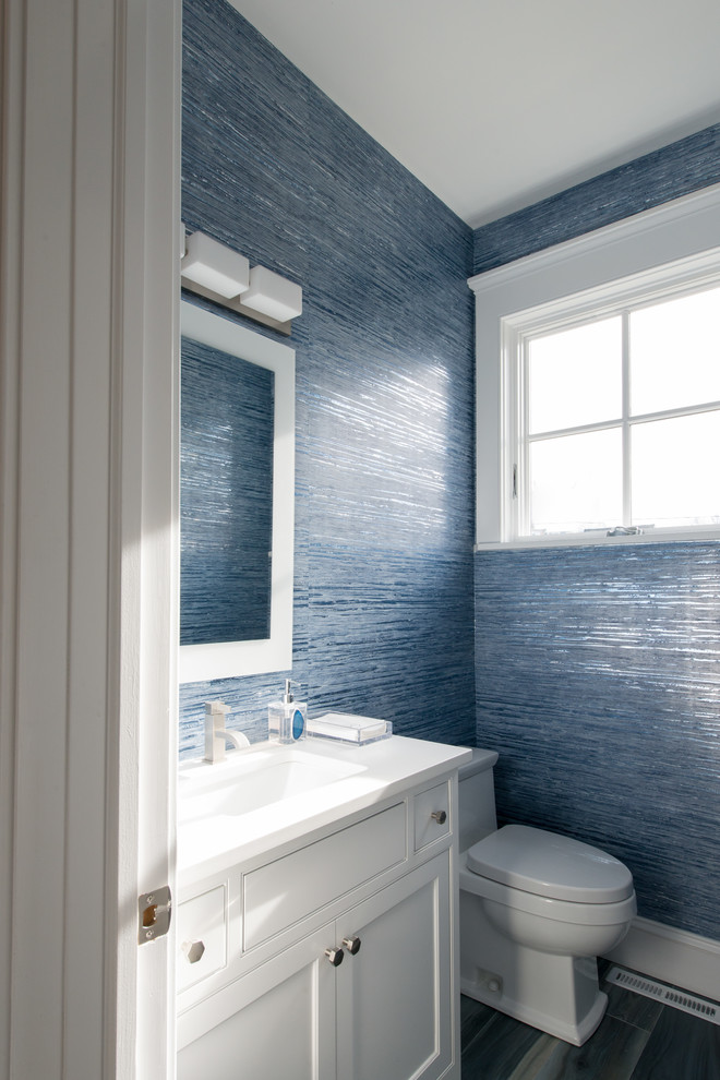 Example of a minimalist porcelain tile and blue floor powder room design in New York with recessed-panel cabinets, white cabinets, a one-piece toilet, blue walls, an undermount sink and quartz countertops