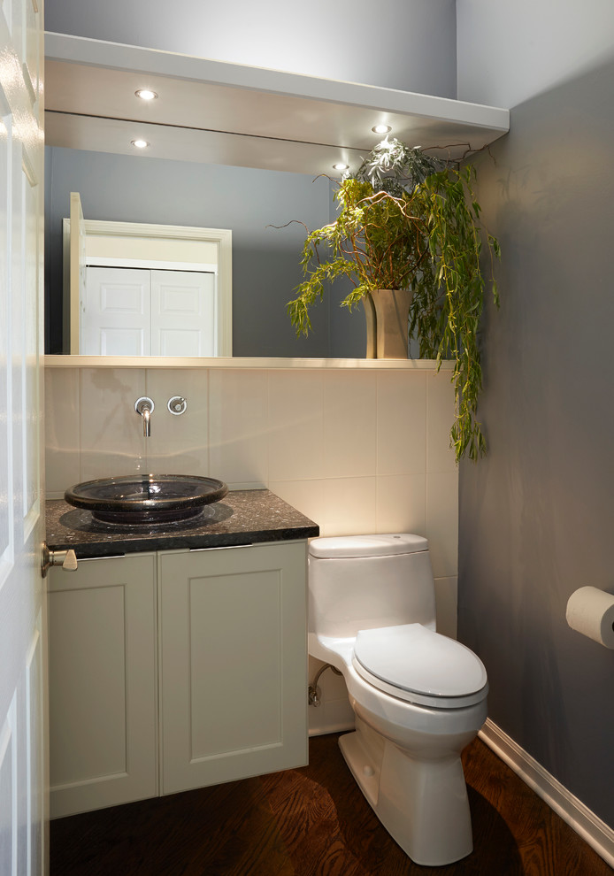 Design ideas for a small contemporary cloakroom in Chicago with recessed-panel cabinets, white cabinets, a one-piece toilet, white tiles, ceramic tiles, blue walls, dark hardwood flooring, a vessel sink, granite worktops and black worktops.