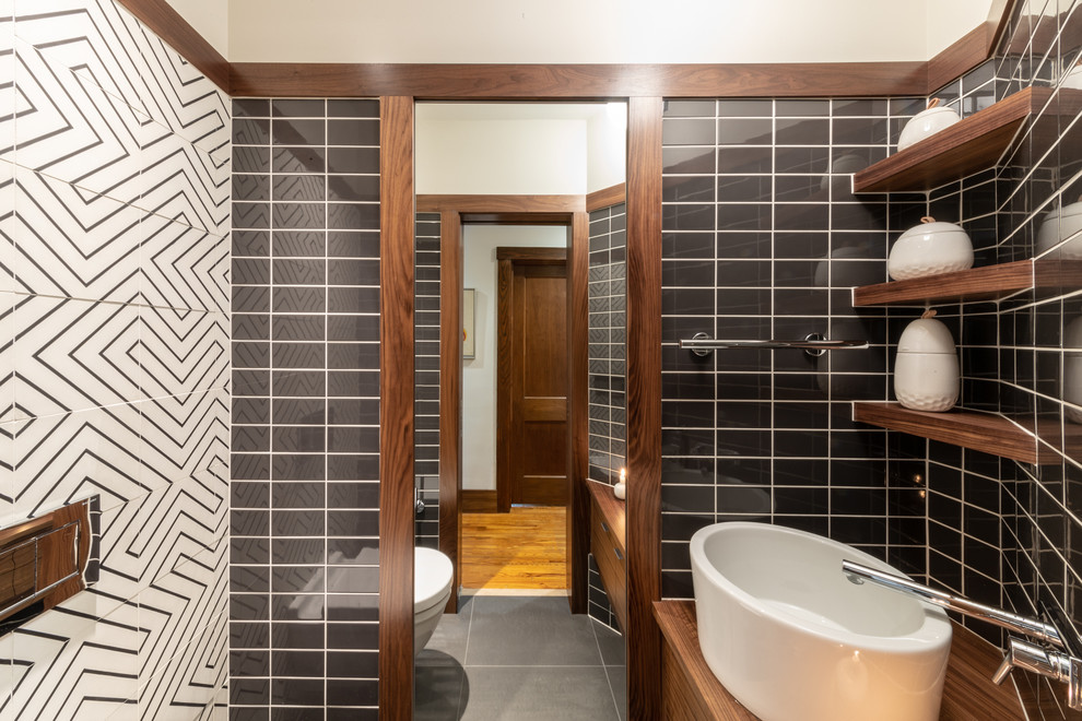 Example of a small minimalist black and white tile and ceramic tile ceramic tile and black floor powder room design in Cedar Rapids with flat-panel cabinets, dark wood cabinets, a one-piece toilet, white walls, a vessel sink, wood countertops and brown countertops