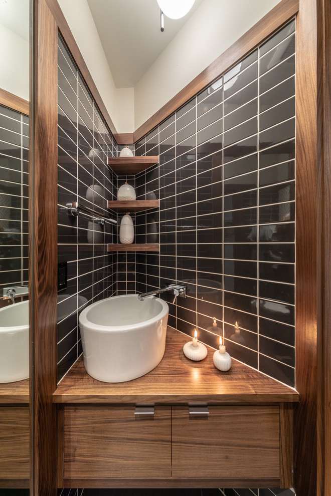 Photo of a small modern cloakroom in Cedar Rapids with flat-panel cabinets, dark wood cabinets, a one-piece toilet, black and white tiles, ceramic tiles, white walls, ceramic flooring, a vessel sink, wooden worktops, black floors and brown worktops.