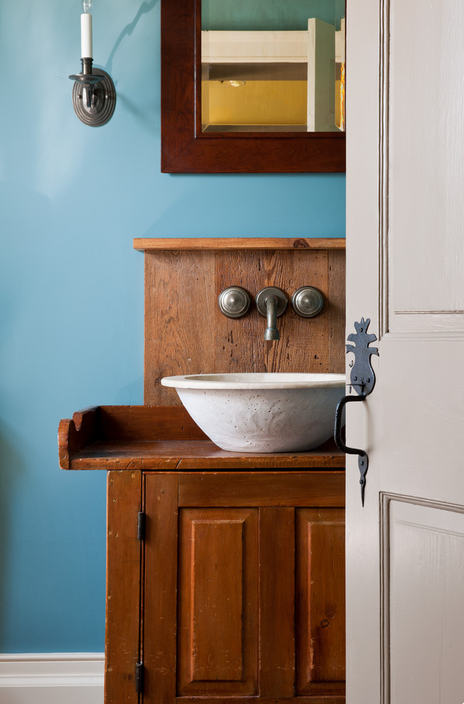 Diseño de aseo campestre con lavabo sobreencimera, armarios con paneles con relieve, puertas de armario de madera oscura y paredes azules