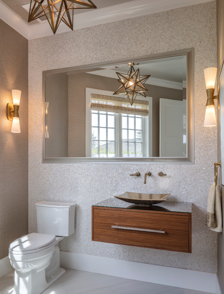 Beach style cloakroom in Sacramento with flat-panel cabinets, dark wood cabinets, a two-piece toilet, beige tiles, beige walls, a vessel sink, glass worktops and grey floors.